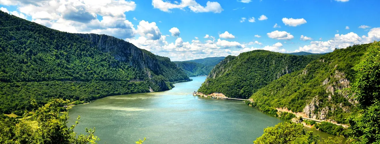 Fluss zwischen steilen, bewaldeten Felshängen unter blauem Himmel