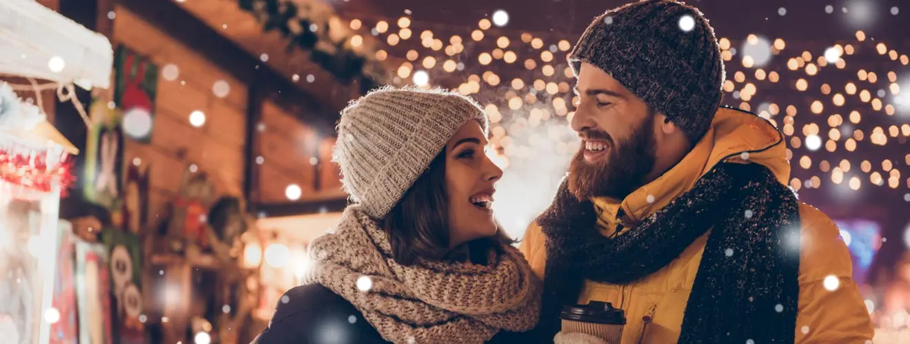 Paar mit Mützen und Schals auf einem beleuchteten Weihnachtsmarkt