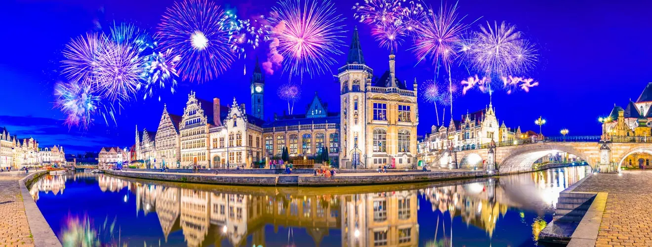 Silvesterfeuerwerk über einer beleuchteten historischen Altstadt am Fluss mit Spiegelungen im Wasser