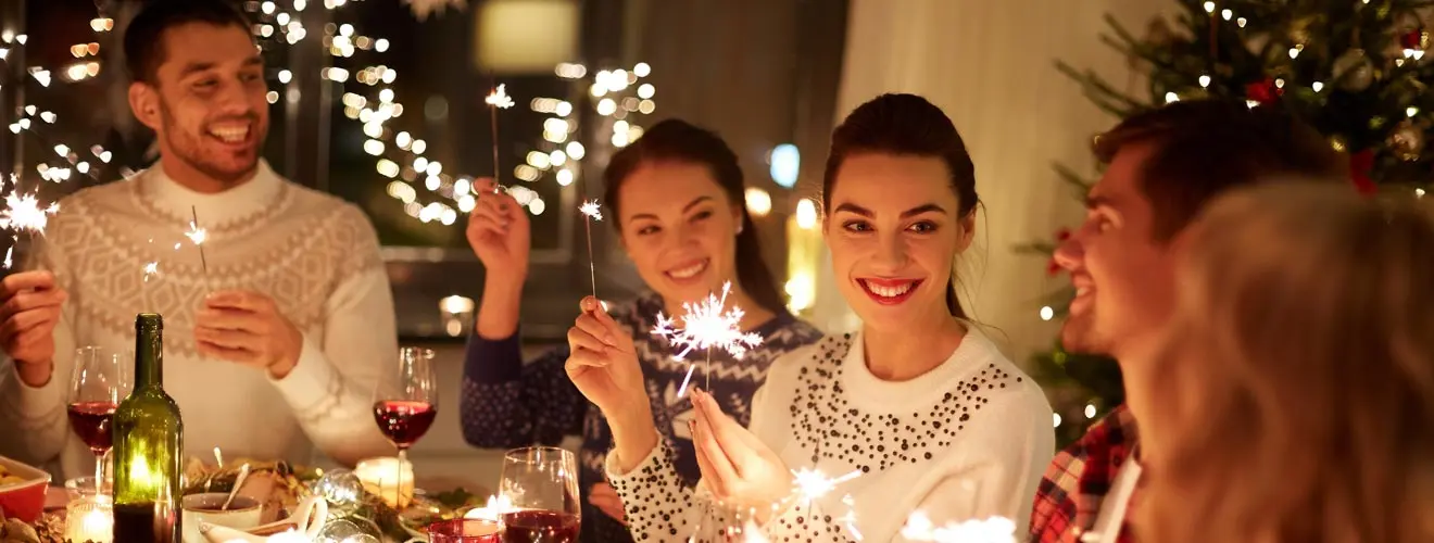 Menschen mit Wunderkerzen an einer weihnachtlich gedeckten Tafel