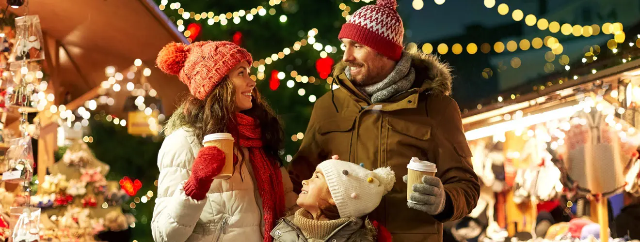 Paar mit Getränkebechern und kleinem Hund auf einem Weihnachtsmarkt