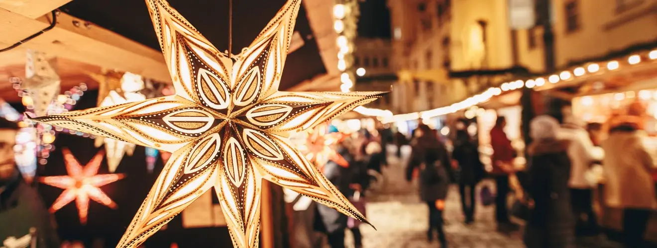 Leuchtender Weihnachtsstern vor Ständen und Besuchern auf einem Weihnachtsmarkt