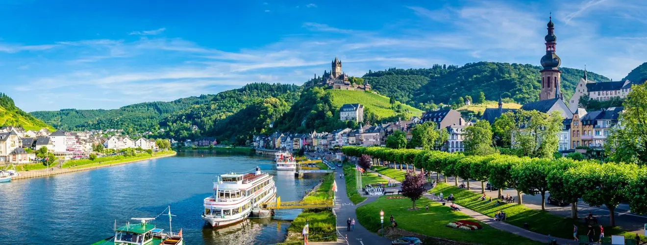 Reichsburg Cochem über der Altstadt mit Schiffen am Moselufer unter blauem Himmel
